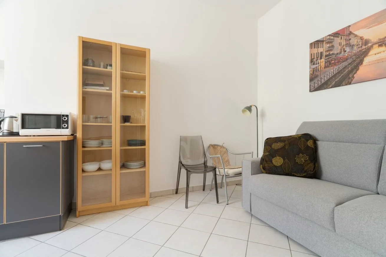A living area with a gray sofa, glass-front cabinet, and small dining table.