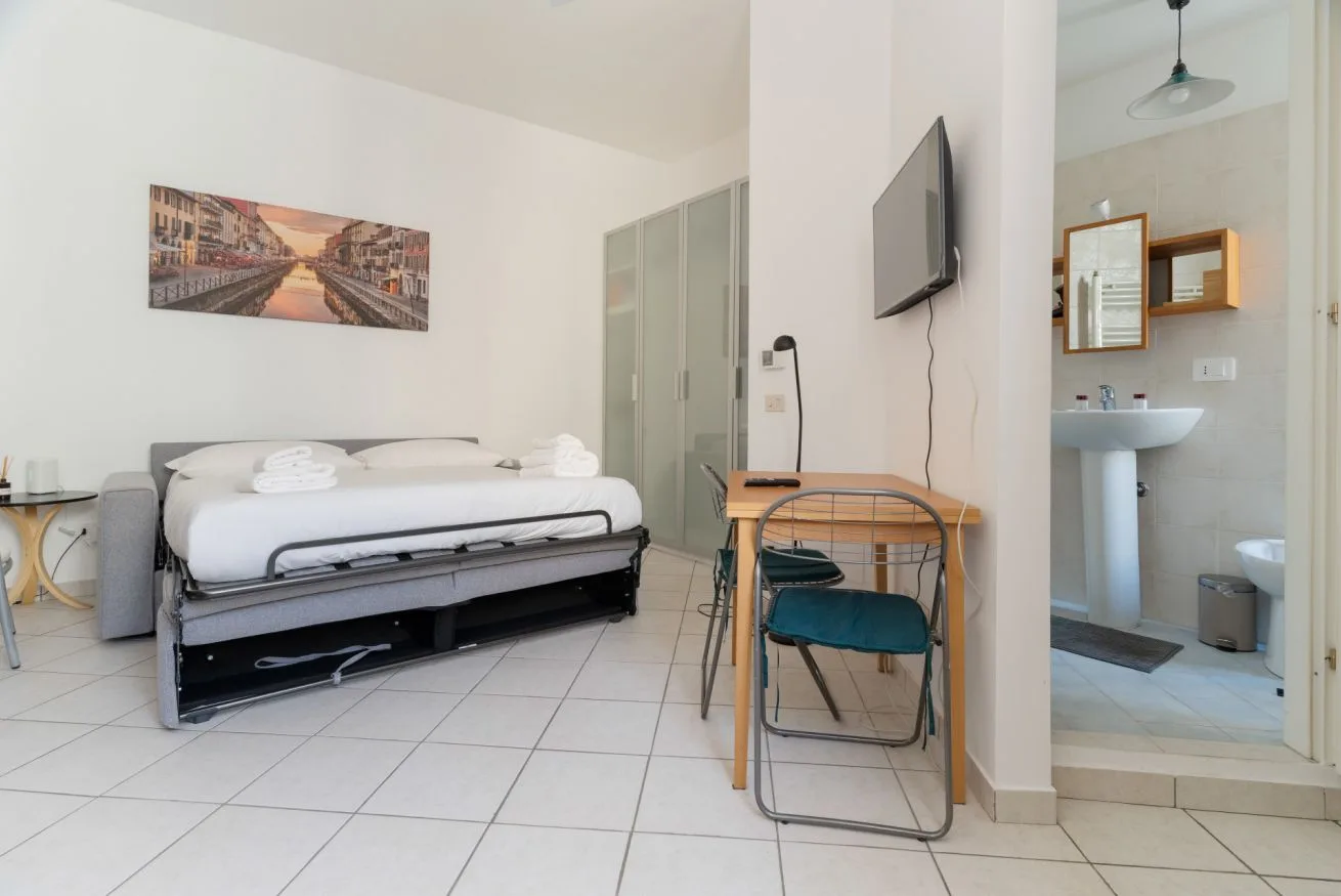 A bedroom with a bed, desk, and an open view into the bathroom.