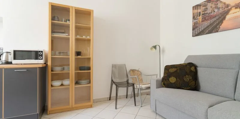 A living area with a gray sofa, glass-front cabinet, and small dining table.