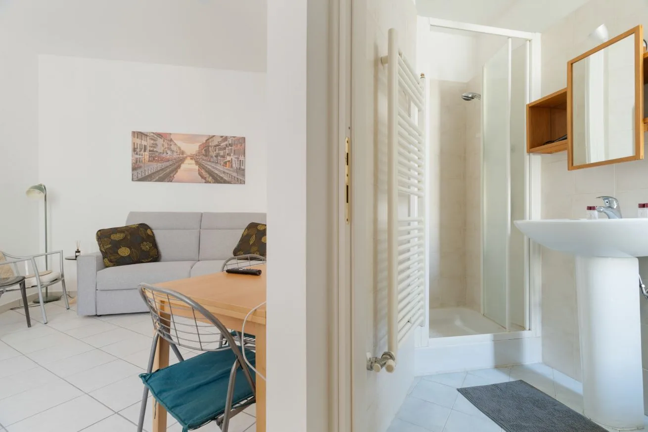 A bright living and dining area opens beside a bathroom with a shower and sink.