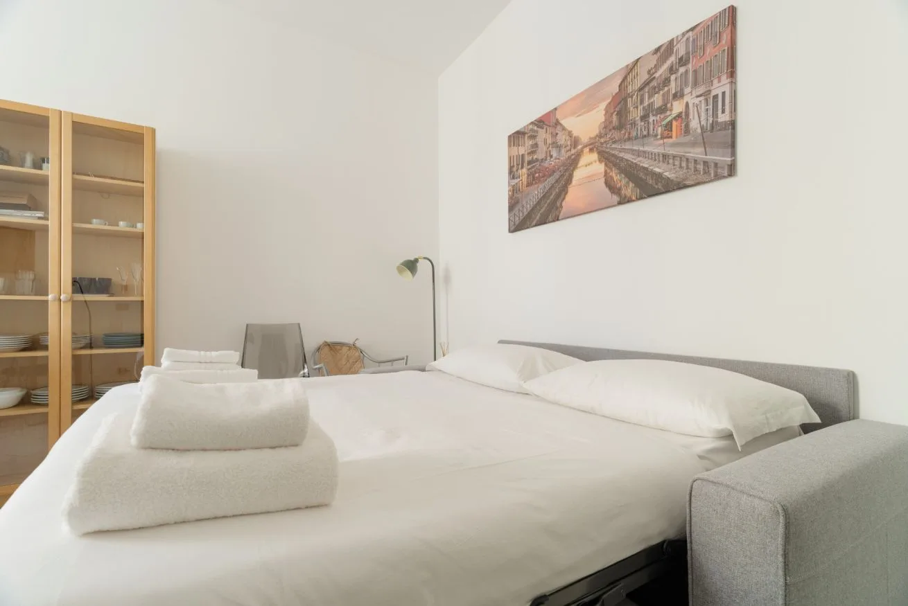 A bedroom with a neatly made bed and a framed cityscape above it.
