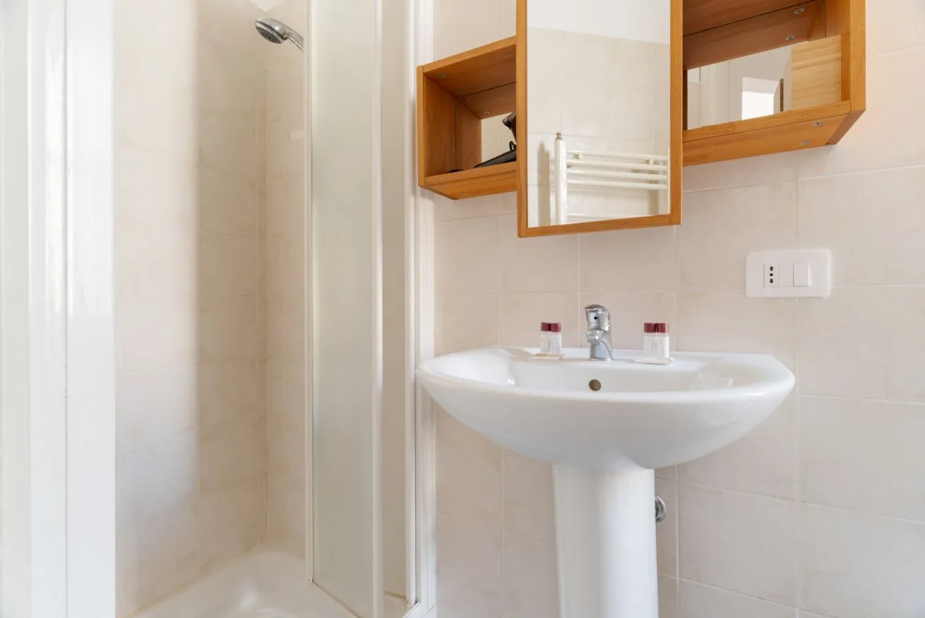 A bright bathroom with a pedestal sink, mirror, and shower.