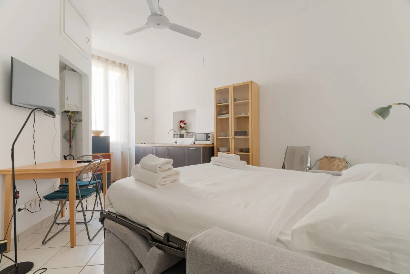 A bright bedroom with a neatly made bed and a desk beside the window.