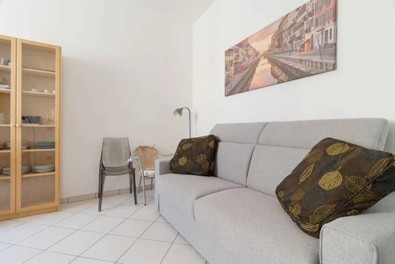 A living room with a gray sofa, patterned cushions, and a framed cityscape.