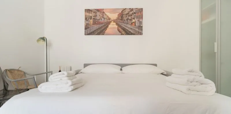 A neatly made bed with folded towels sits beneath a framed wall picture.