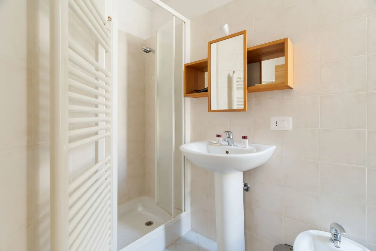 A tiled bathroom with a pedestal sink, mirror, and shower.