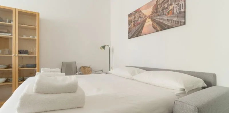 A bedroom with a neatly made bed, bedside lamp, and wall art.