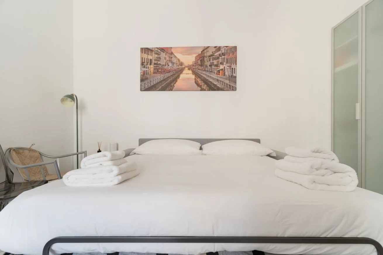 A bedroom with a neatly made bed and folded towels on either side.