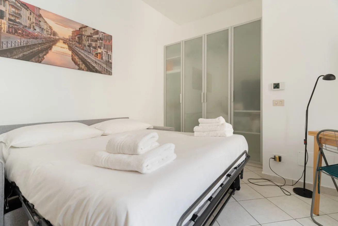 A bright bedroom with a neatly made bed and folded white towels.