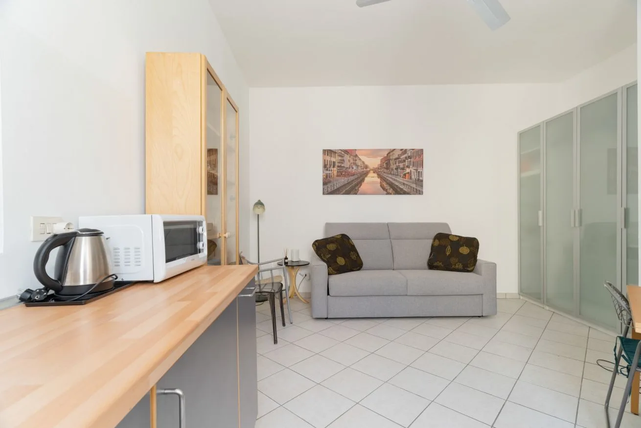 A bright room with a gray sofa, a kitchenette counter, and glass-fronted cabinets.