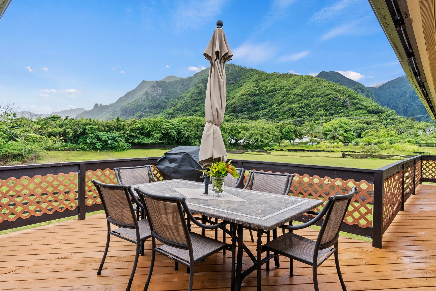 A patio dining area with a table and chairs overlooks green hills.