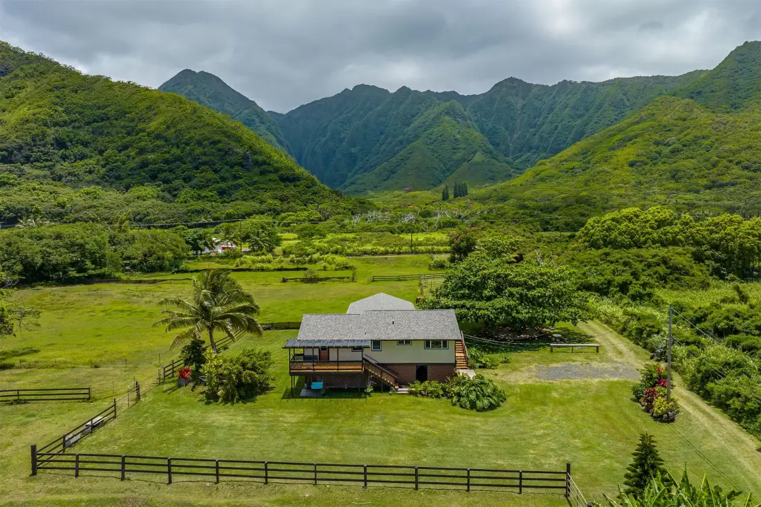 Una casa se encuentra en un valle cubierto de hierba, rodeado de montañas verdes.