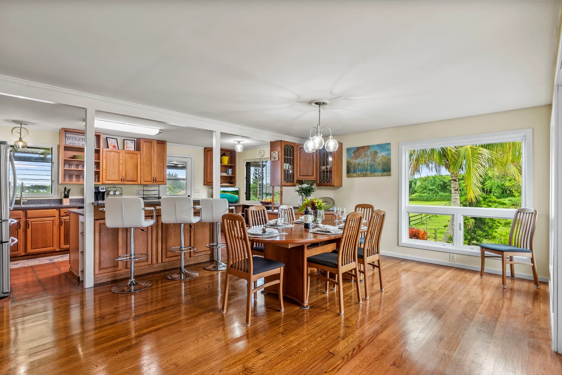Un comedor abierto con una mesa de madera junto a una cocina y grandes ventanas.