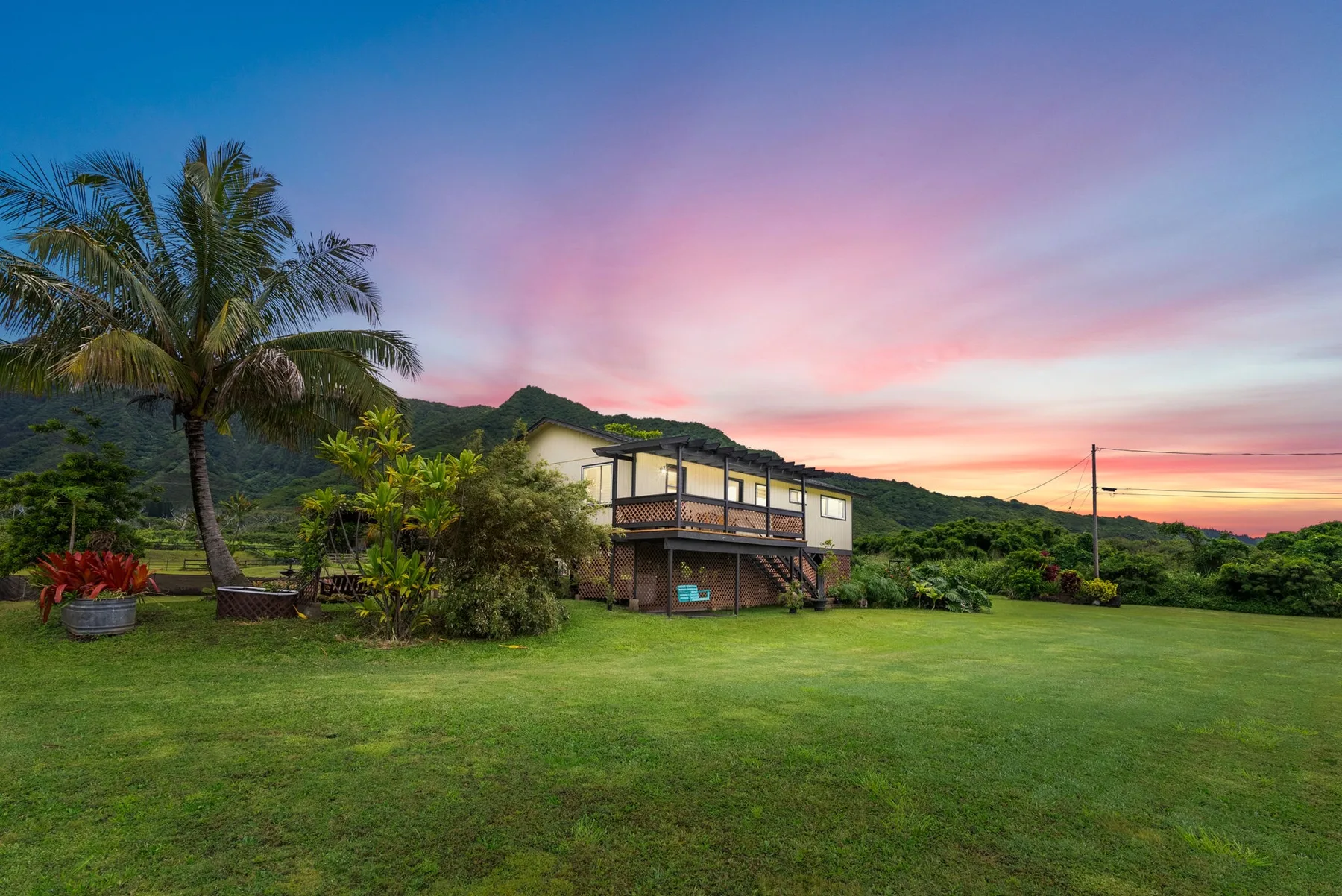 A raised house stands on a broad green lawn beneath a colorful sunset sky.