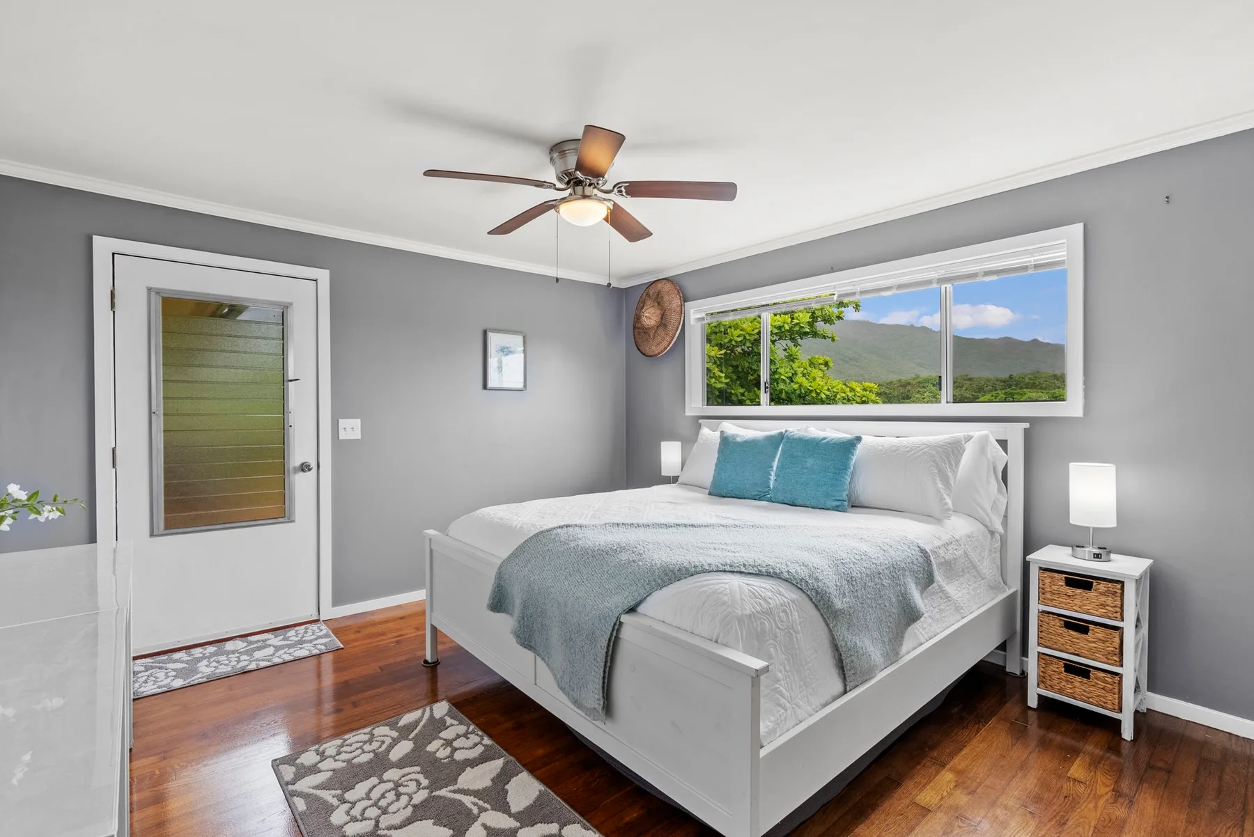 Un dormitorio con una cama blanca, almohadas turquesas y una ventana con vista a la vegetación.