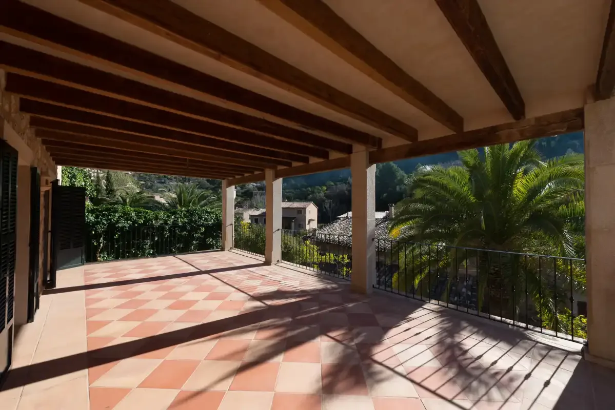 A covered outdoor terrace with patterned tile flooring and views of surrounding greenery.