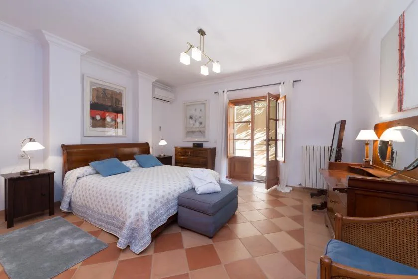A bright bedroom with a double bed, bedside tables, and a glass-paneled door.