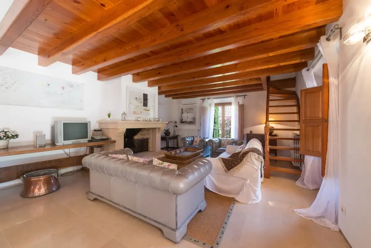 A living room with seating arranged around a fireplace beneath exposed wooden ceiling beams.
