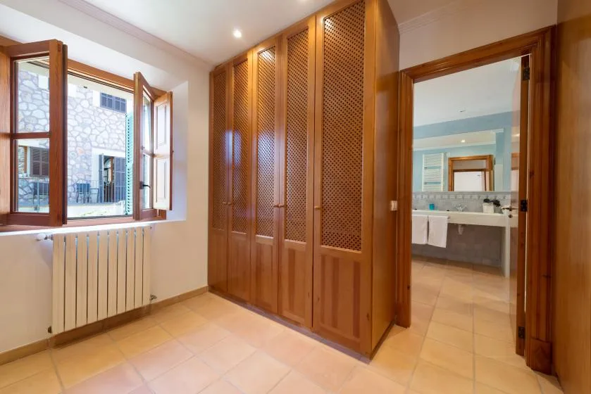 A bedroom with wooden wardrobes, an open window, and a view into the bathroom.