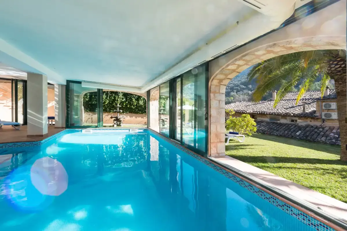 An indoor swimming pool opens onto a grassy garden through glass walls.