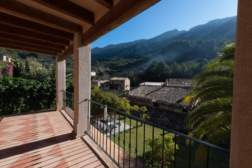 A covered balcony overlooks nearby rooftops and a green mountain landscape.