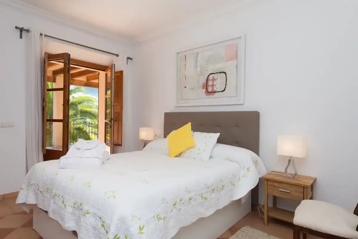 A bright bedroom with a white bed, bedside lamps, and open wooden windows.