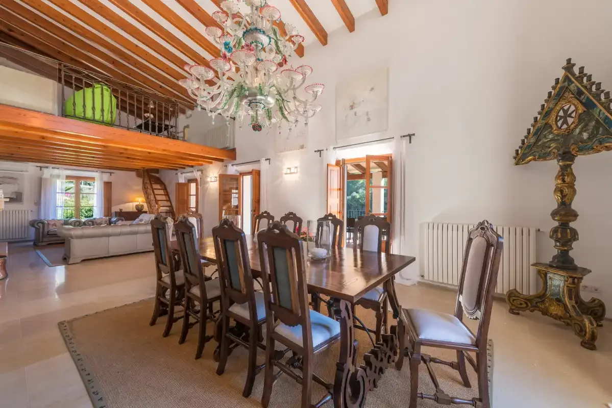 A dining area with a long table and chairs beneath a wooden-beamed ceiling.