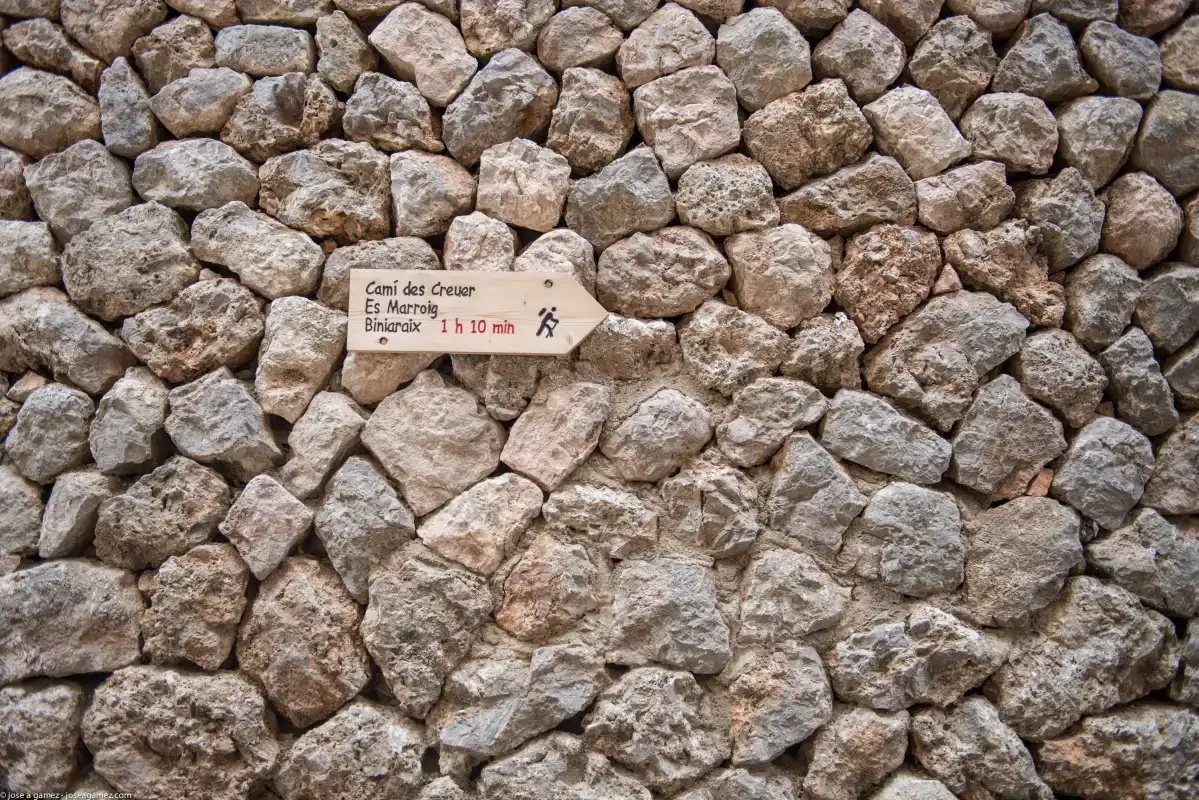A stone wall with a small hiking trail sign attached.
