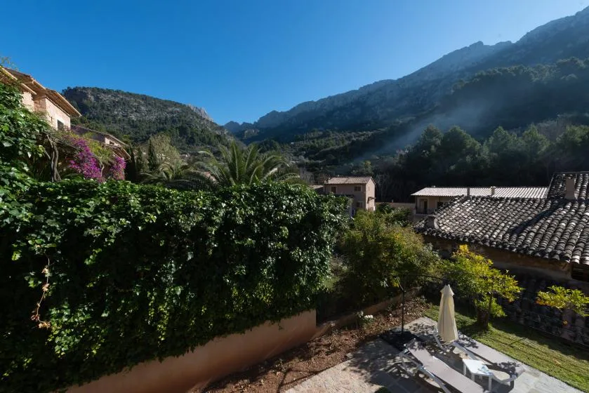 A landscaped outdoor terrace overlooks tiled rooftops and a green mountain valley.