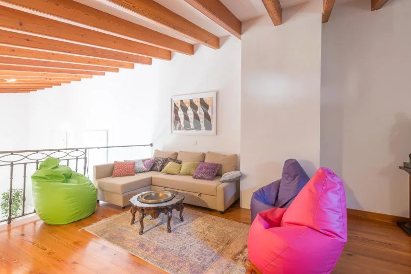 A bright living room with a sectional seating area, colorful beanbags, and exposed ceiling beams.