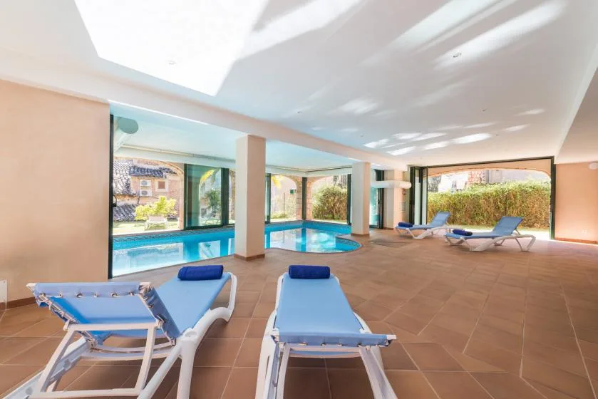 An indoor pool area has blue lounge chairs beside large windows.