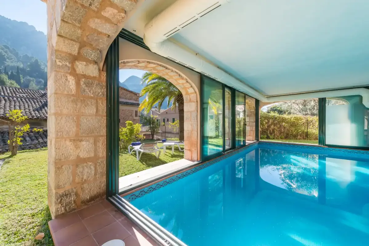 An indoor swimming pool beside large windows and a stone archway.