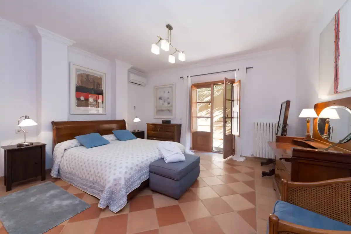 A bright bedroom with a bed, bedside tables, and an open doorway to a balcony.