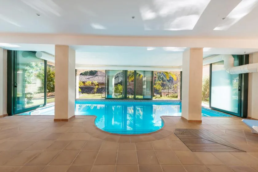 An indoor swimming pool is surrounded by tiled flooring and large windows.