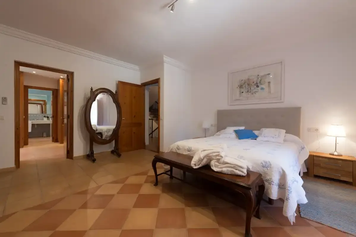 A bedroom with a bed, a wooden bench, and tiled flooring.