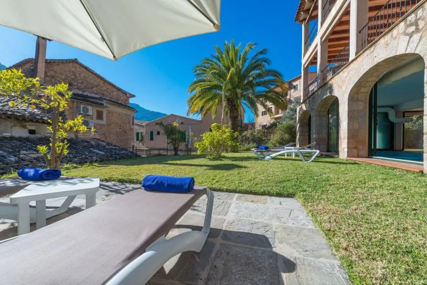 A sunny courtyard with lawn, palm trees, and outdoor lounge seating beside a building.