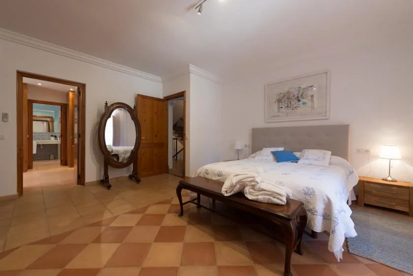 A bedroom with a large bed, a wooden bench, and an oval standing mirror.