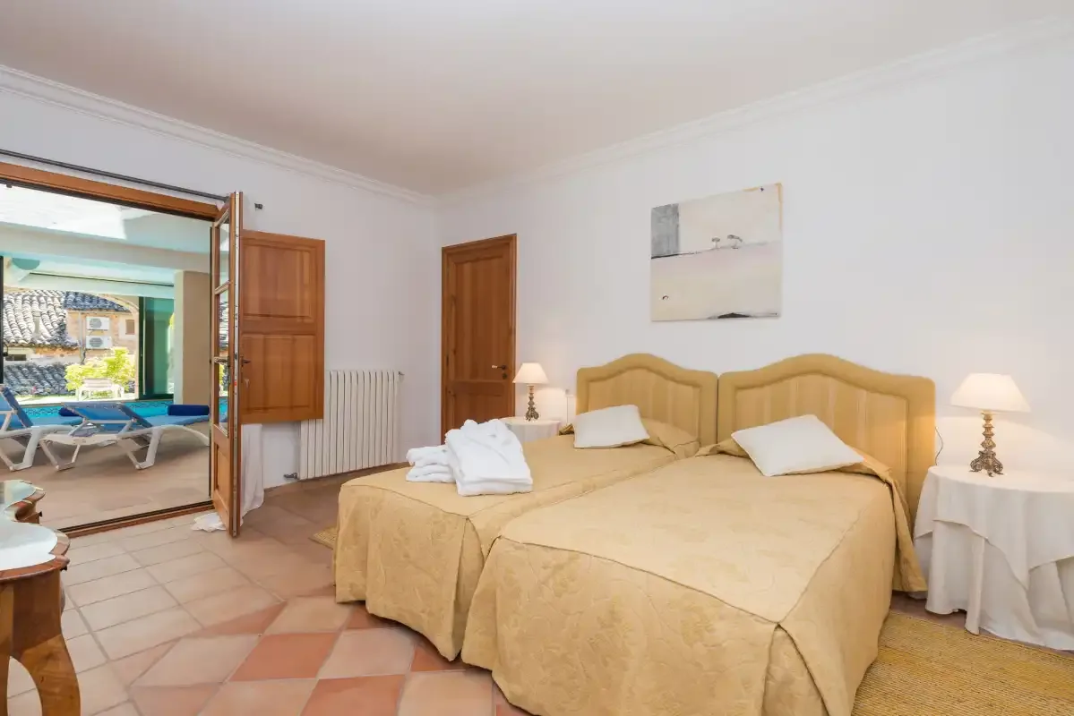 A bright bedroom with two beds and an open doorway to a terrace.