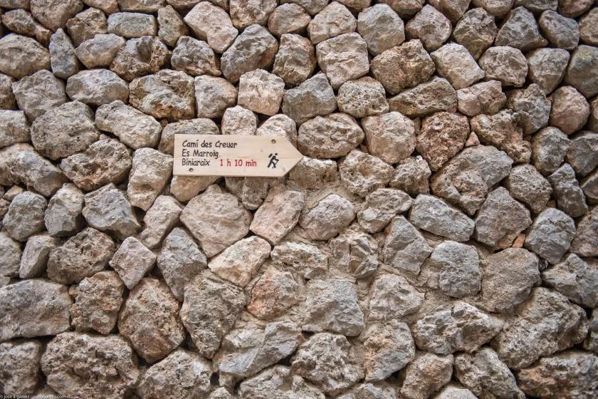 A stone wall with a small hiking trail sign.