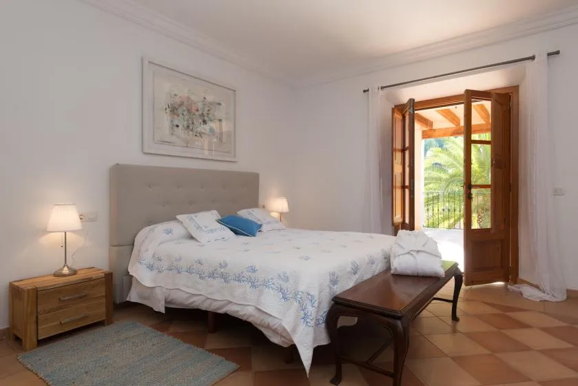 A bedroom with a double bed, bedside tables, and an open balcony door.