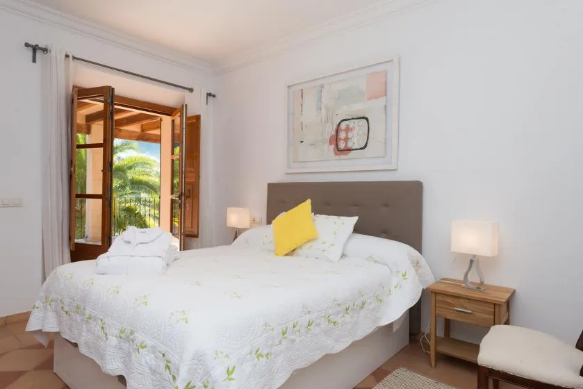 A bedroom with a neatly made bed and an open window overlooking greenery.