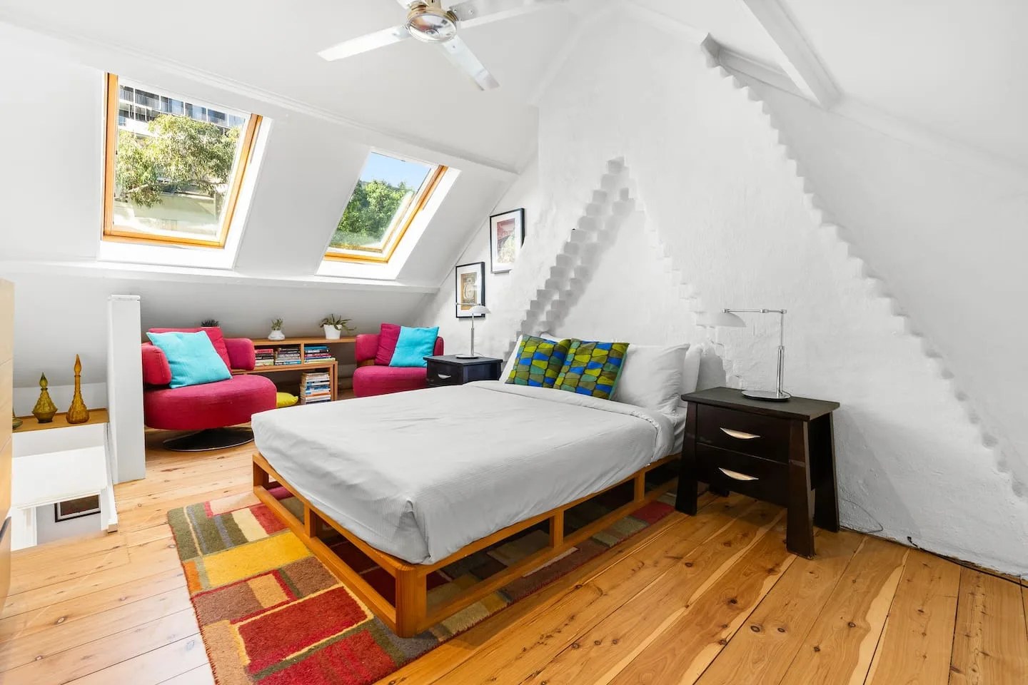 A loft bedroom with a large bed, colorful seating, and sloped ceilings.