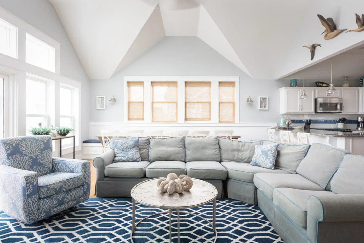 A bright living room features a sectional sofa and a blue patterned rug.