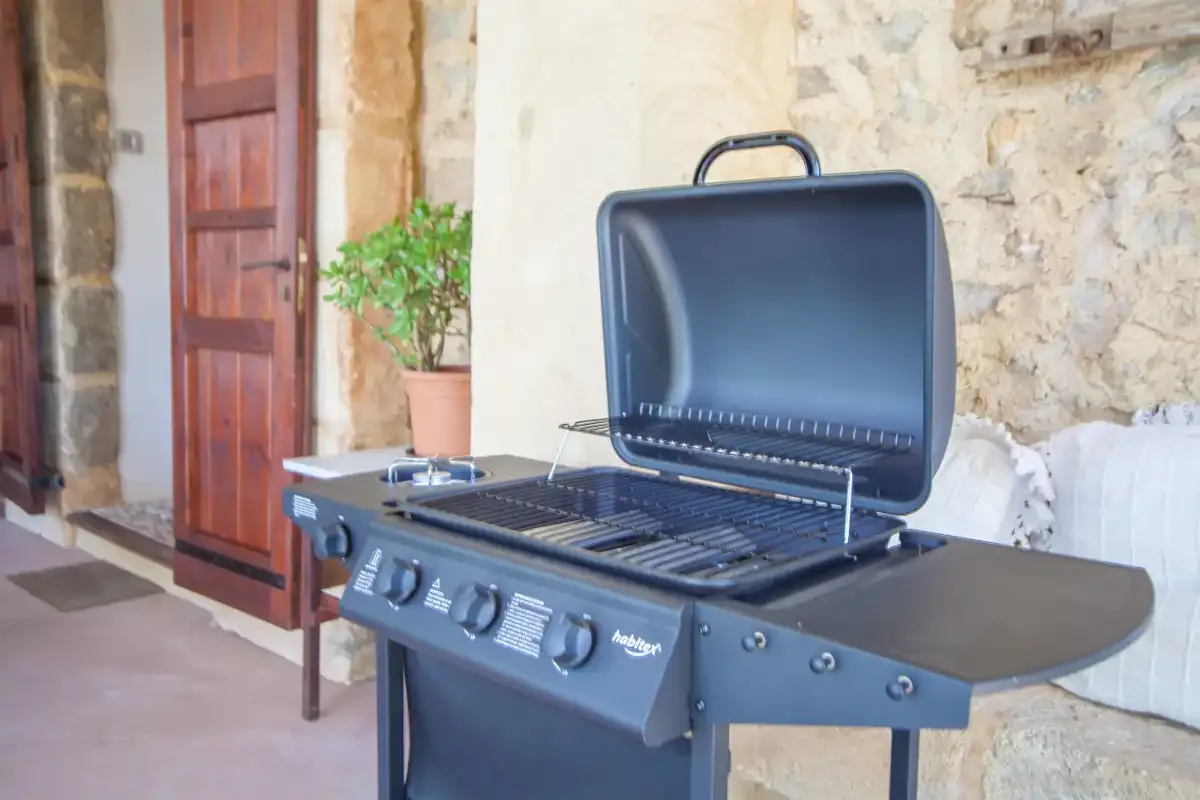 An outdoor grill stands beside a stone wall and wooden doorway.