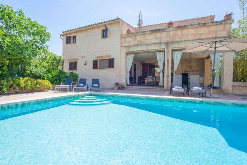 A swimming pool beside a house with a shaded outdoor seating area.