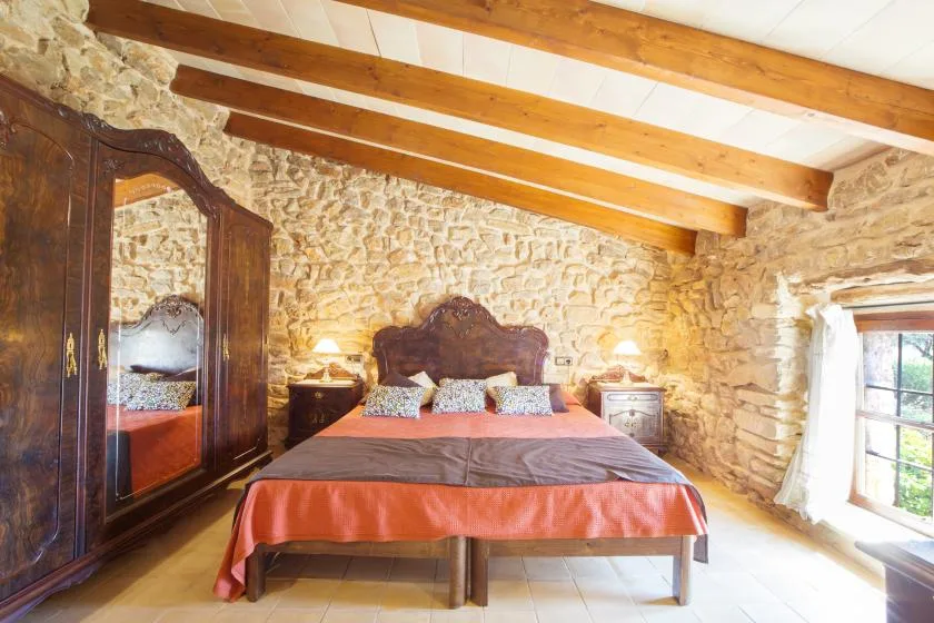 A bedroom with a large bed, wooden wardrobe, and exposed stone walls.