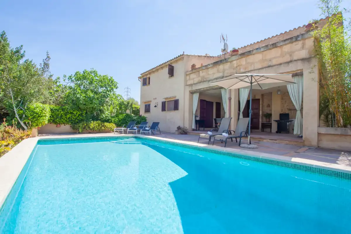 A swimming pool beside a house, with patio seating under a canopy.