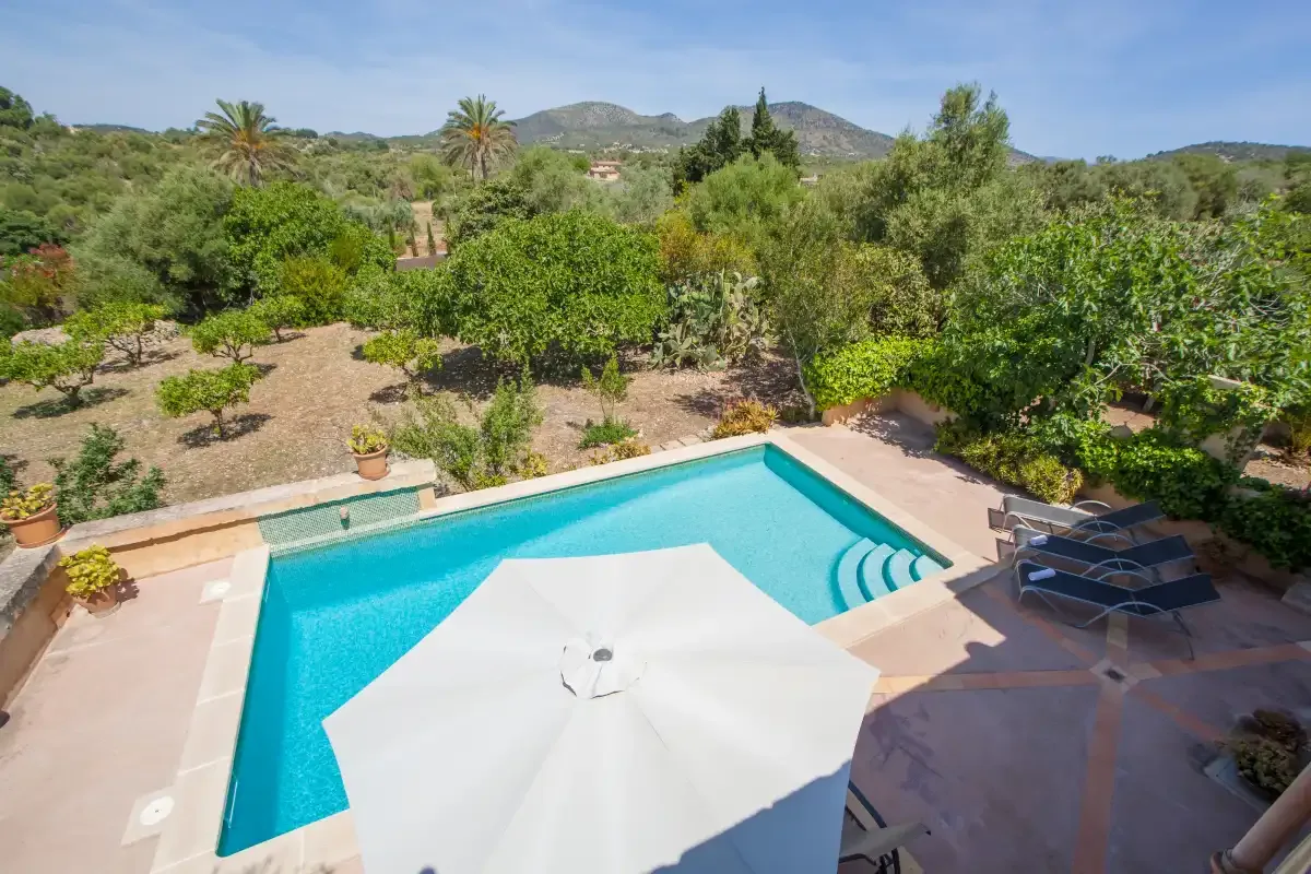 A swimming pool and patio sit among green gardens with hills in the distance.
