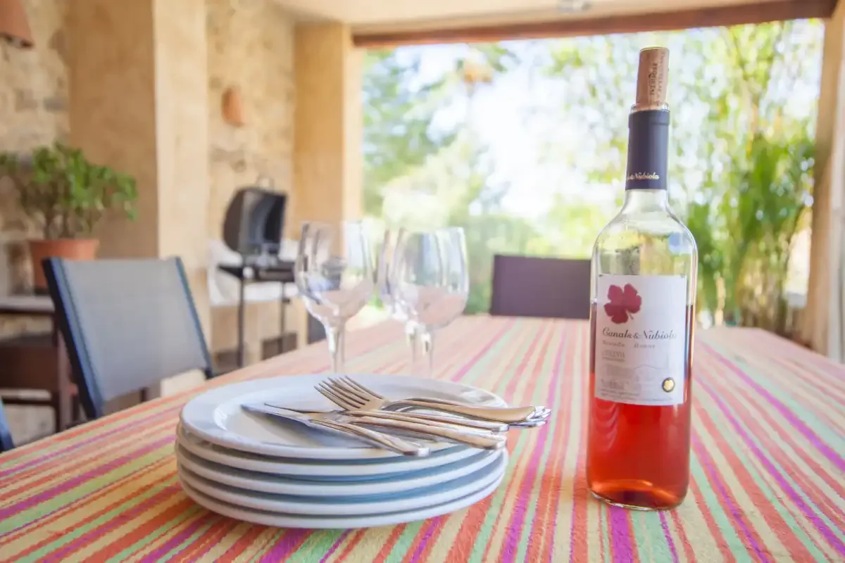 A dining table is set with plates, glasses, and a bottle beside an open patio.