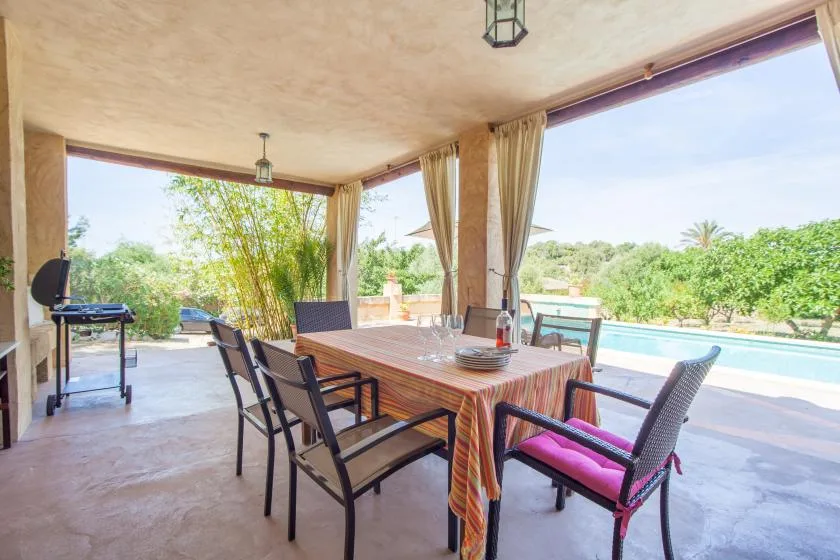 A covered patio dining area overlooks a pool and greenery.